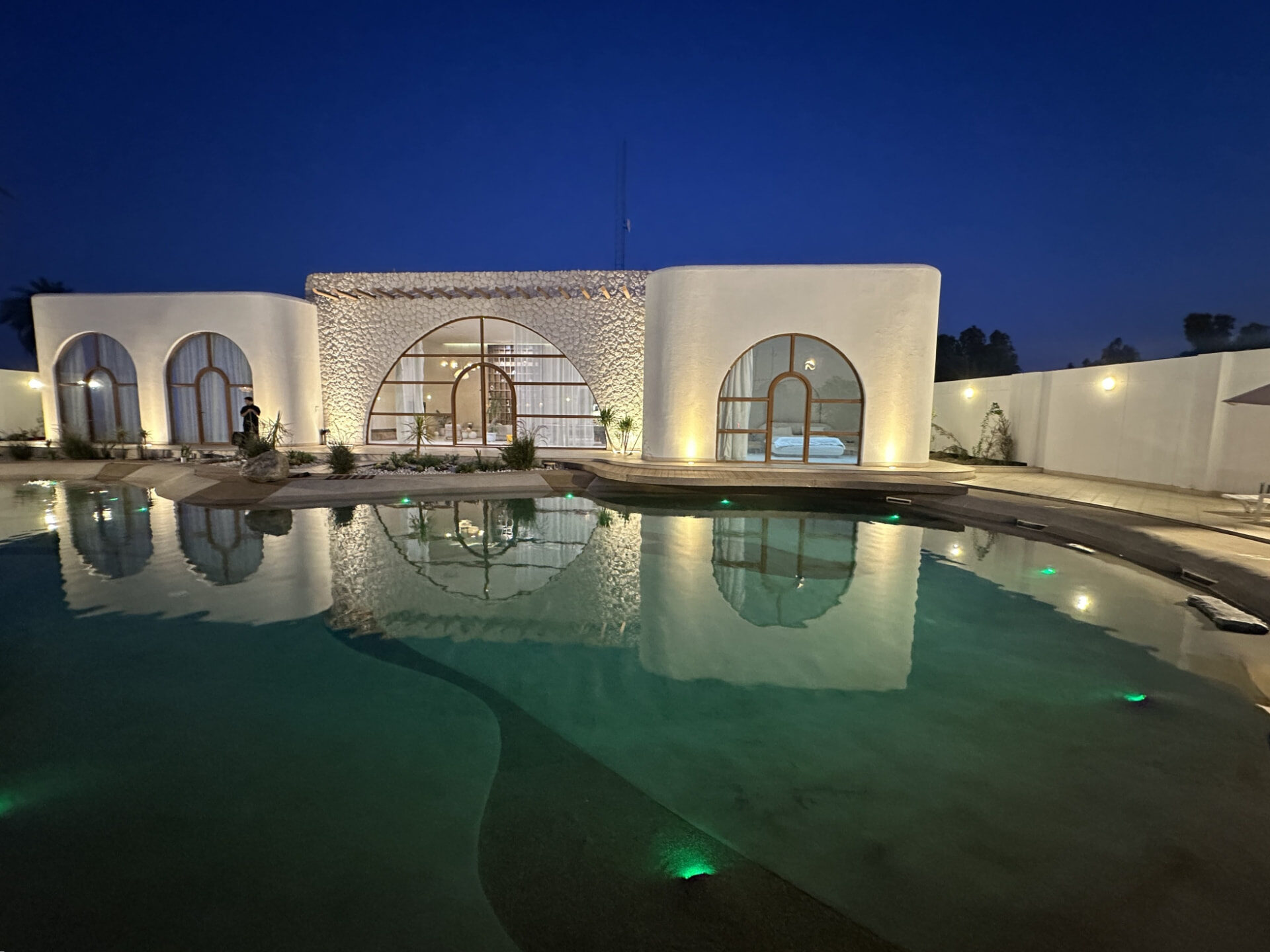 Completed lagoon pool and lit villa with stone edging and planting at dusk