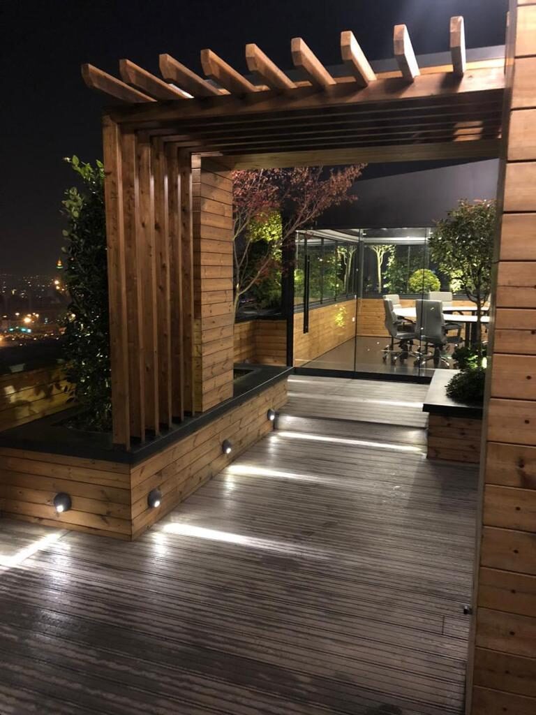 Illuminated timber pergola, bench seating and decking on a rooftop at night