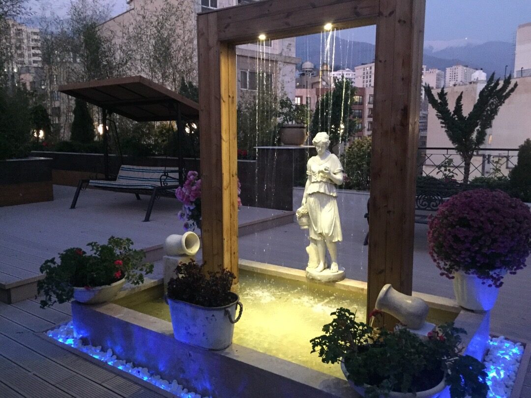 Timber-framed water curtain with a stone basin, pebbles and seasonal flowers at dusk