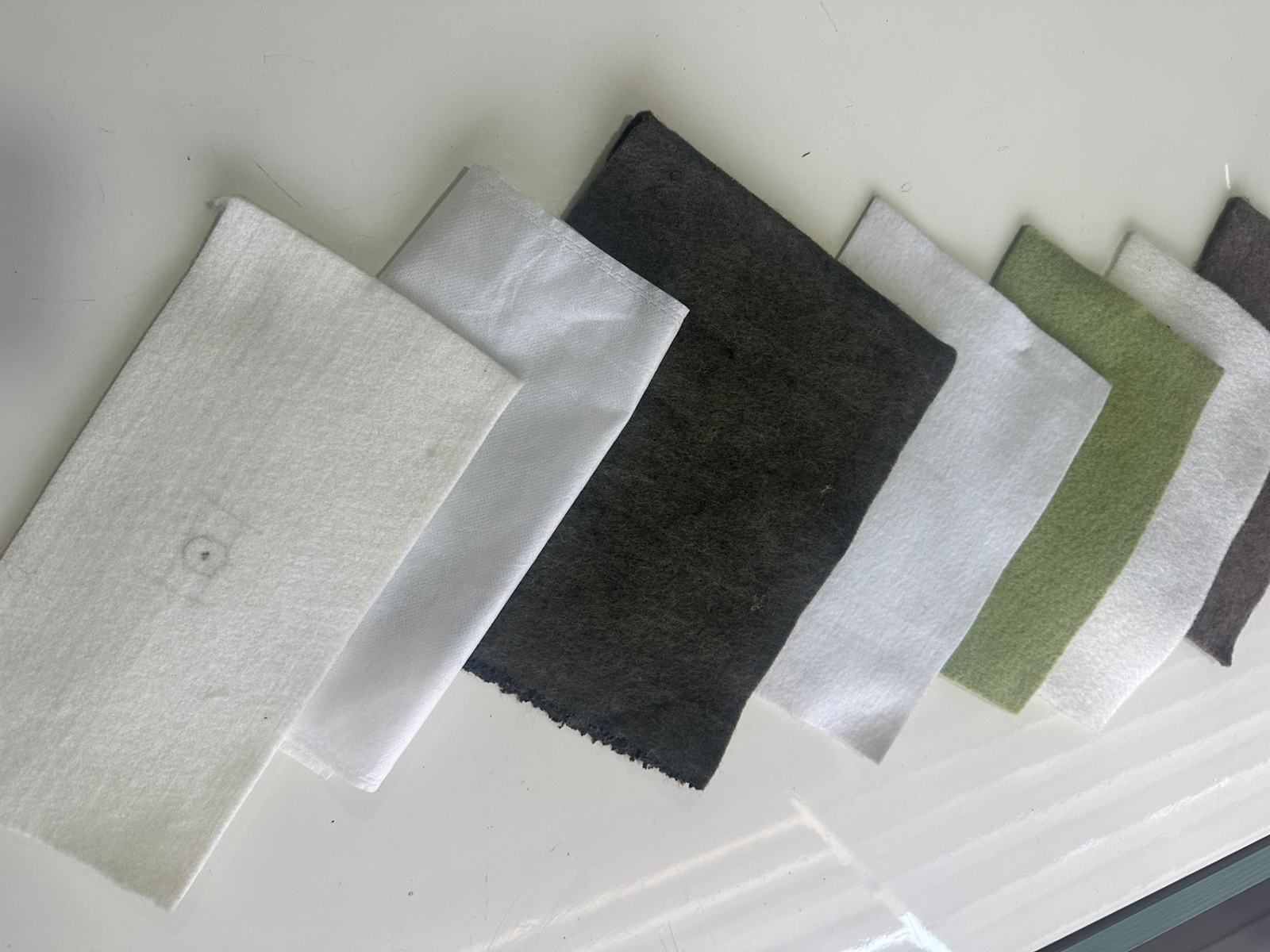 Geotextile fabric samples in white, grey and green weights